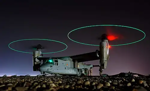 Ground crew refuel an MV-22 before a mission in central Iraq at night. The rotors are turning and the tips are green, forming green circles.
