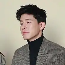 Kim facing right and wearing a black turtleneck and striped blazer.