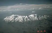 An elongated snow-covered ridge rises from a dark landscape with valleys.