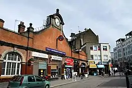 A brown-bricked building with a rectangular, blue sign reading "HAMMERSMITH STATION" in white letters all under a grey sky