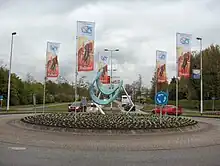 A roundabout with a sculpture in the middle of it, and banners depicting cyclists hanging around it