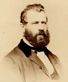 Sepia photo of Turcotte, half-profile head and shoulders; dark hair and beard, wearing mid-Victorian business suit