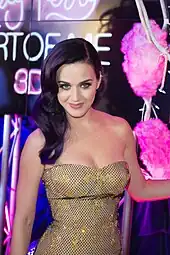 With shoulder-length violet hair and cartilage piercing on her right ear, A Caucasian female in a yellow and black polka-dotted bustier smiles with her head tilted slightly forward.