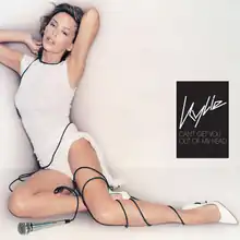 A woman is posing while wearing a white dress and high heels. A wired microphone is wrapped up on her left leg. A black box featuring the words 'Kylie' and 'Can't Get You Out of My Head' in white is placed on the right.