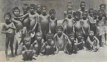A group of 15 boys, 10 standing and five squatting. Most appear naked. All have prominent pot-bellies but ribs obviously showing, a common symptom of malnutrition.
