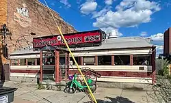 A single-story building in the shape of a railroad car, with an Art Deco facade in cream and maroon stripes situated next to a taller brick building