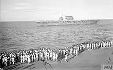Black and white photo of men standing on the deck of a ship looking at another ship which is sailing nearby