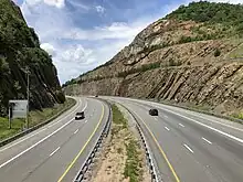 A highway passes through a cut through a mountain. The rock walls of the cut are visible above the highway.