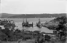 A large warship is tied to the dock in a narrow channel of water.