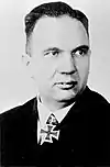 A man wearing a black military uniform with an Iron Cross displayed at the front of his uniform collar.