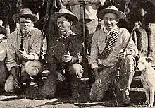 Photo taken in 1893 of three Bulawayo field scouts kneeling in front of their horses. Bob Bain on the left, Burnham in the middle, Maurice Gifford and his dog on the right.  Burnham is dressed in his Arizona clothes and is holding his Winchester model 1873 .44WCF rifle