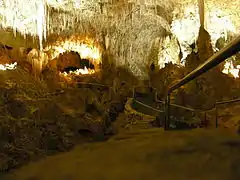 A picture of a partially illuminated cave with a jagged rock ceiling and a walkway extended into the cavern.