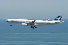 A white A330 over water, marked with Cathay Pacific and its logo on the vertical stabiliser, gear extended