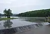 Water from a forest-surrounded lake spills over a stairstep dam