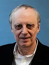 A white male in his early 70s, grey hair receding, wearing a black jacket.