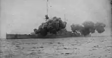 A large warship is partially obscured by smoke from its main guns firing.