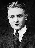 Photograph of F. Scott Fitzgerald as a student at Princeton. The photo features only his head and shoulders. He is wearing a dark tie and a pin-striped suit.  His hair is parted in the middle and neatly coiffed.