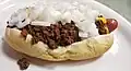 A hot dog sausage topped with beef chili, white onions and mustard