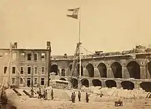 1861 photograph of the interior of a damaged military fortification. The flag of the Confederate States of America flies from a flagpole near the center of the photograph.