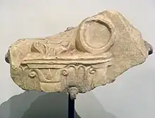 Photograph of a fragment of white marble sculpture, showing a tripod sculpted in bas-relief.