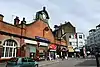 A brown-bricked building with a rectangular, blue sign reading "HAMMERSMITH STATION" in white letters all under a grey sky