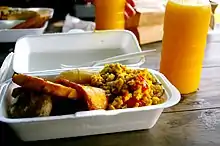 A Styrofoam container of food, plastic fork, and glass of juice