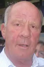 An old balding man looks directly into the camera