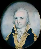 A man with stringy, gray hair wearing a navy jacket with gold epaulets and collar and a high-collared white shirt gathered at the neck