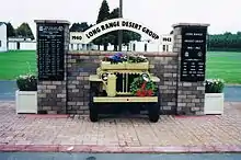 Front end of a jeep, sticking out of brick wall with plaques on brick pillars either side