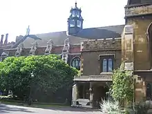 A long, low building of brick and stonework, with arched windows. It is partially obscured by trees and shrubs. The slate roof features a six-sided tower of stone and glass.