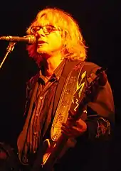 Mike Mills plays bass guitar and sings into a microphone