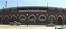 A large brick stadium with many round windows on the bottom and many rectangle windows in groups of four line the top of the stadium. The words Modern Woodmen Park are displayed above the door