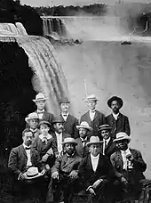 A dozen African American men seated with Niagara Falls in the background