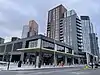 A low grey building with a projecting canopy stands in front of tall residential buildings