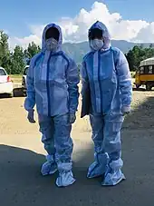Two paramedics wearing medical PPE gowns outdoors.