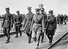A general walks in military uniform flanked by other officers