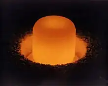 Glowing cylinder of plutonium oxide standing in a circular pit