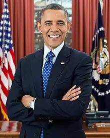 Obama standing in the Oval Office with his arms folded and smiling