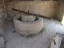 A reconstructed olive press from Volubilis consisting of a circular stone basin with a circular stone inset, atop which a long wooden bar is fixed