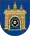 A coat of arms depicting a grey castle with three towers topped by crosses with a human head on the front door all on a blue background