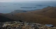 A view from a high rocky eminence with brown moorland below and a vista of small brown islands scattered in the sea beyond. A low bank of fog obscures the horizon.