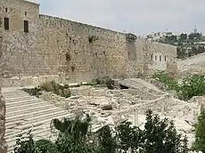 The long southern wall of Jerusalem's Temple Mount rises above two flights of stone steps between which are some low ruins