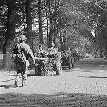 Men on foot and jeeps towing guns on a tree lined road