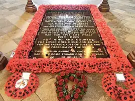 A black tombstone surrounded by red poppies with three wreaths at its foot.