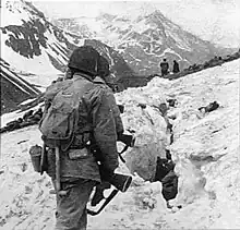 A line of soldiers hiking on the side of a snow-covered mountain, viewed from behind