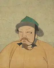 Portrait of a man with a long thin beard and mustache, wearing an orange robe and a small green hat with fur.